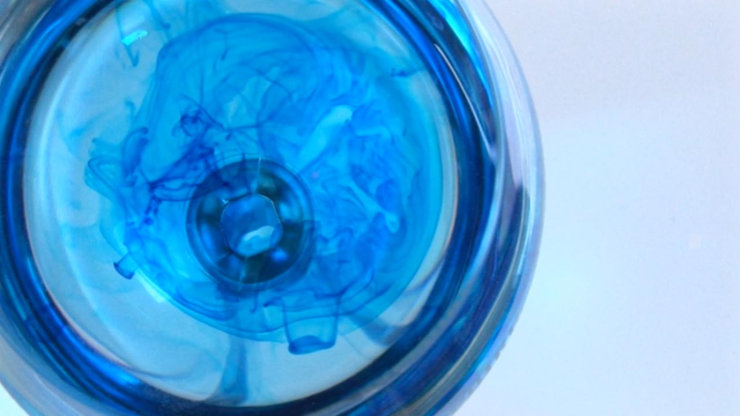 Contagious, a still from an art video showing blue ink dispersing in clear liquid, forming fluid, organic shapes that radiate from the center, suggesting spread, transformation, and subtle motion.